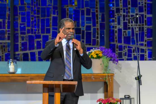 A preacher in a black suit preaching on faith and prayer.