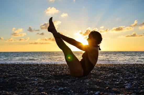 A fitness enthusiast woman doing v-ups on a beach at sunset.