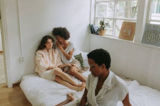 wo women sitting next to the wall gossiping while another sits a lone.