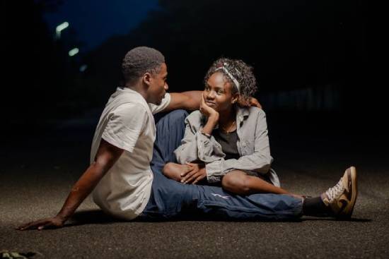 A couple sitting on a street at dusk looking at each other.