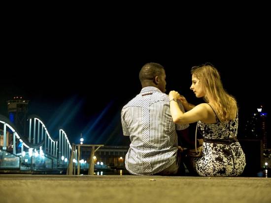 A couple sitting side by side on a platform at night having a safe conversation.