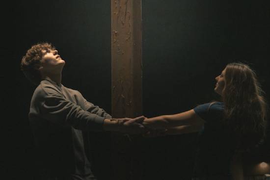 A couple playing a relationship bonding game by holding hands around a wooden beam.