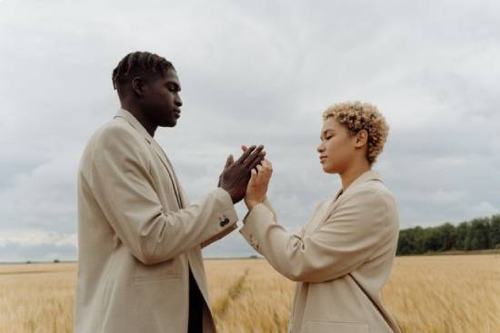 A couple in beige suits holding hands and having safe conversations in a grassfield.