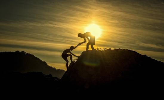 Silhouette of a Helpful Friend Silhouette of a person helping a friend climb a steep terrain.