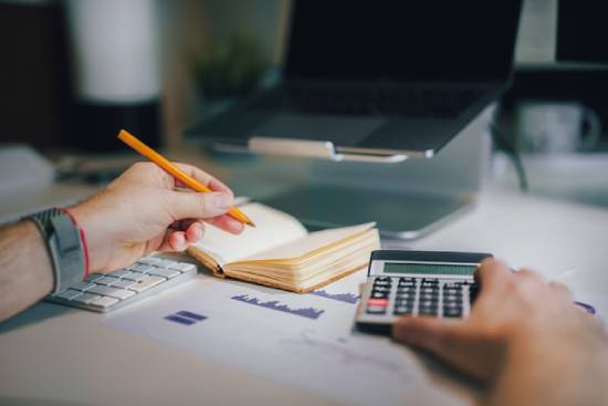 A person sitting on a working desk with a calculator and notebook writing a personal budget.