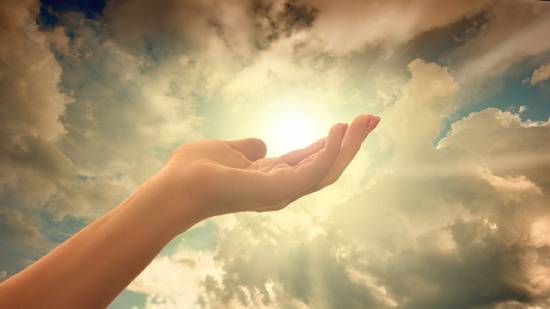 Divine Light Presence Hand lifted towards divine light in the sky.
