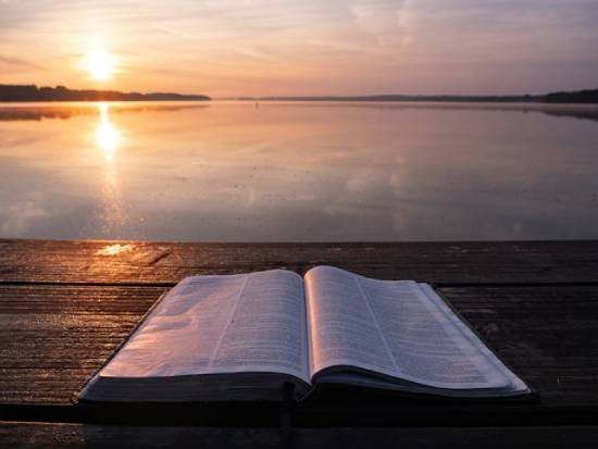 Open Bible on a Table by the Seashore An open Bible placed on a table by seashore at sunrise.