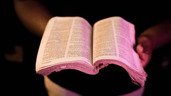 A person holding an open Bible in the light at night. A person holding an open Bible in the light at night.