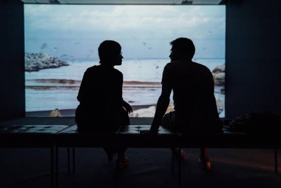 Silhouette of a Couple Having a Talk Silhouette of a couple sitting on a bench by a window facing the sea talking.