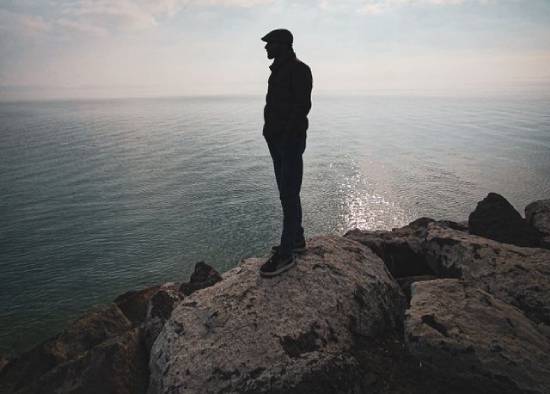 Silhouette of a Man Standing on a Rocky Seaside Silhouette of a man standing on a rock on a rocky seaside in deep thoughts facing the sea.