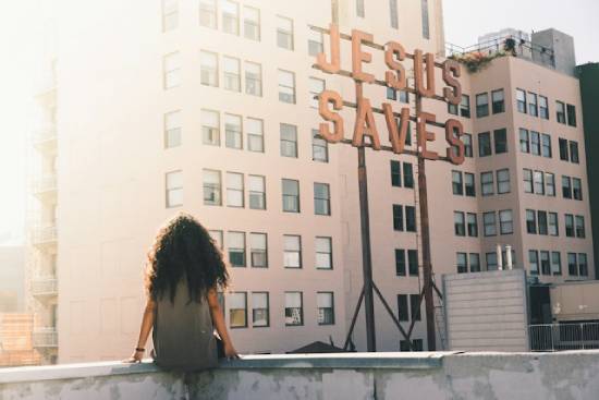 Woman Facing Wall Written 'Jesus Saves'. A woman sitting on a budding edge facing a flat with 'Jesus Saves' writings.